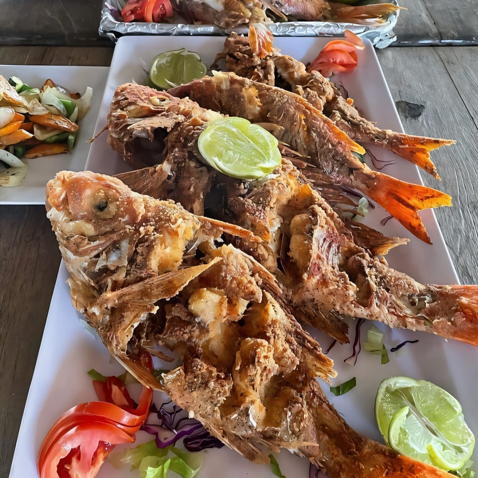 Three whole fried Jamaican escovitch fish with lime and tomato garnishes on white plates.