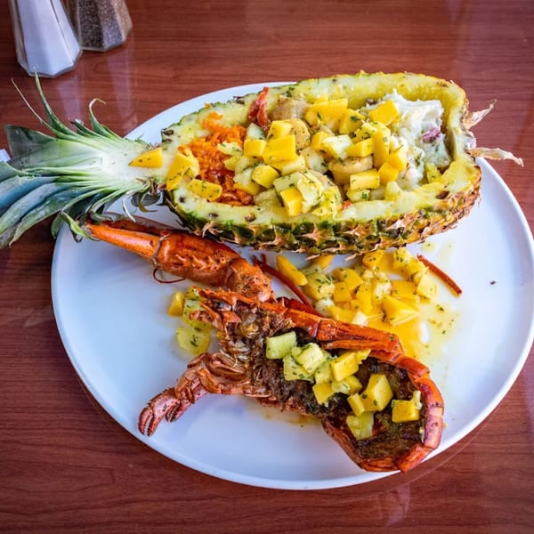 Grilled lobster and pineapple stuffed with rice and mango salsa on a white plate.
