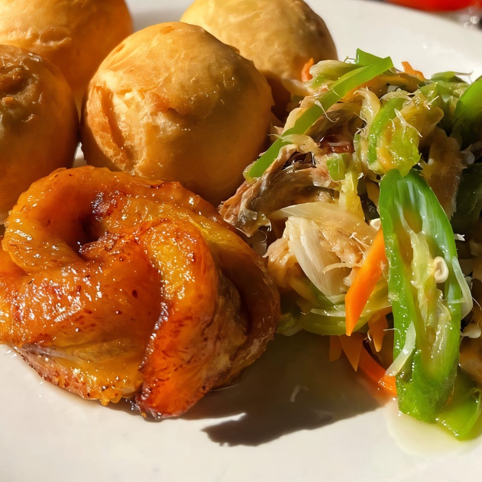 Jamaican fried dumplings, brown stew fish, and escovitch vegetables on a white plate.