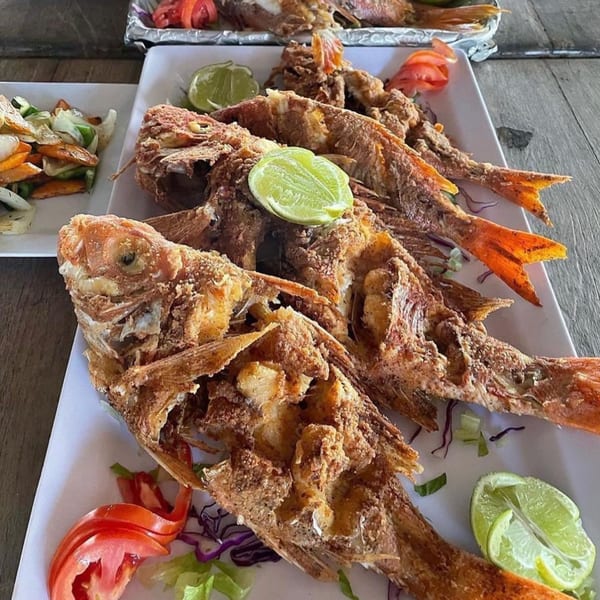 Three whole fried fish with lime wedges and a side salad on white plates.