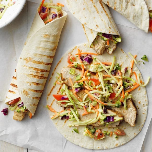 Three Jamaican jerk chicken wraps with colorful slaw and grilled tortillas on white parchment paper.